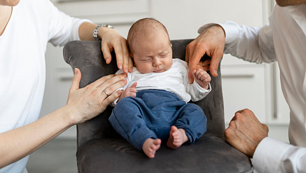 Parents sitting by baby boy sleeping on armchair at home