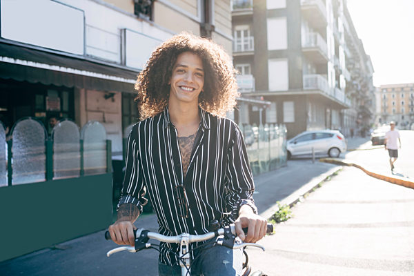 Smiling man with curly hair riding bicycle on street in city during sunny day