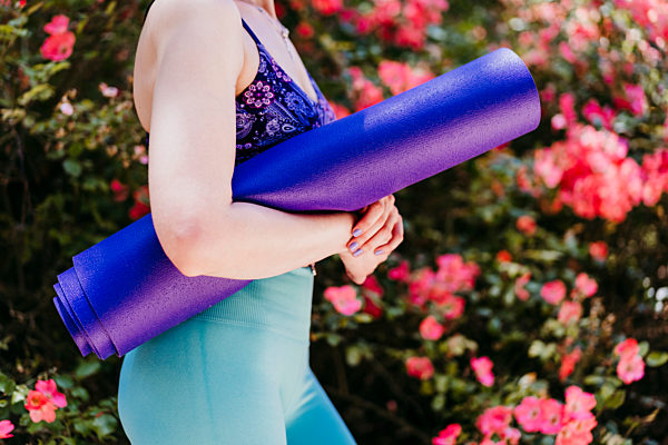 Fit woman with purple yoga mat while standing in park