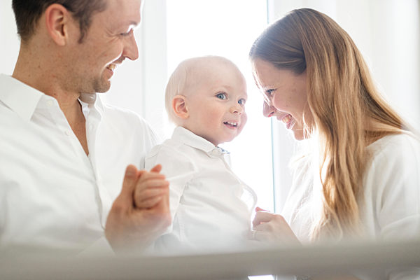 Cheerful parents looking while playing with baby at home