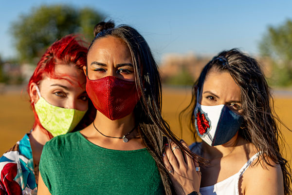 Friends wearing colorful face mask while standing outdoors on sunny day