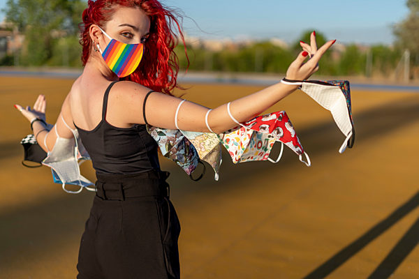 Young woman wearing and hanging face mask while looking over shoulder on sunny day outdoors