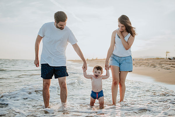 Mother and father with son standing in water at beach during sunset