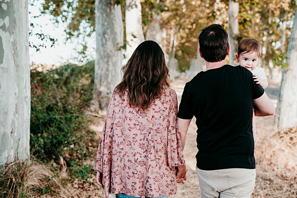 Father carrying baby while holding hand of mother outdoors