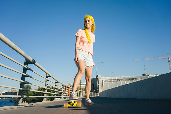 Woman standing on skateboard against clear during sunny day