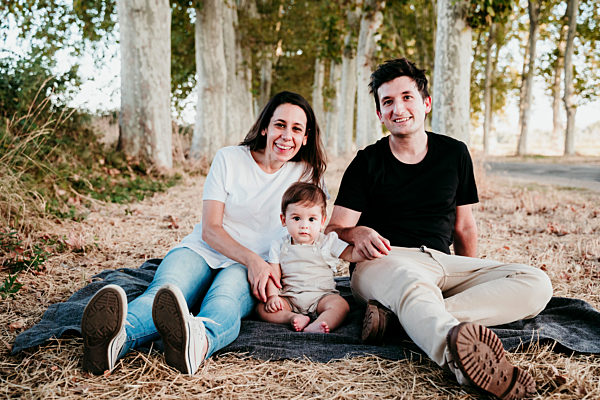 Smiling man and woman sitting with baby boy on blanket outdoors
