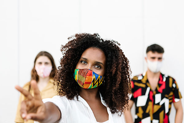 Young woman doing gesture while wearing face mask with friends standing against wall