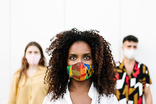 Young woman wearing face mask with friends standing against wall