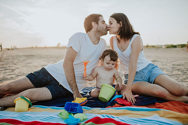 Husband and wife kissing while son playing with toys at beach