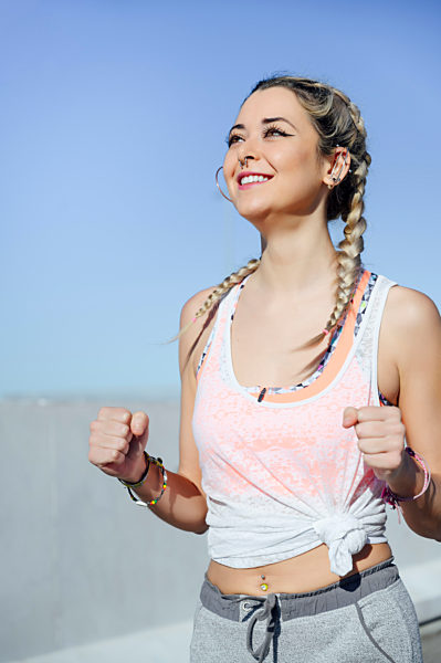 Smiling sportswoman cheering while standing against sky