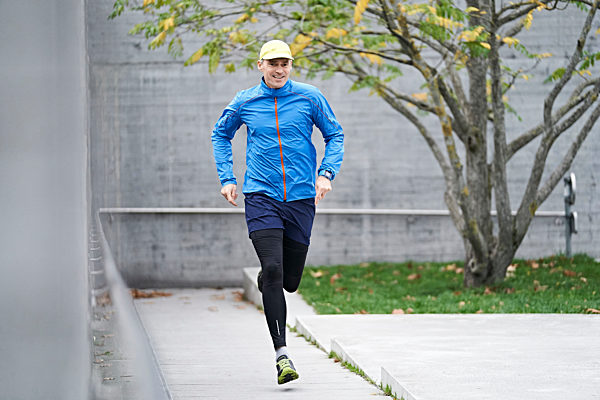Mature man wearing cap jogging on footpath