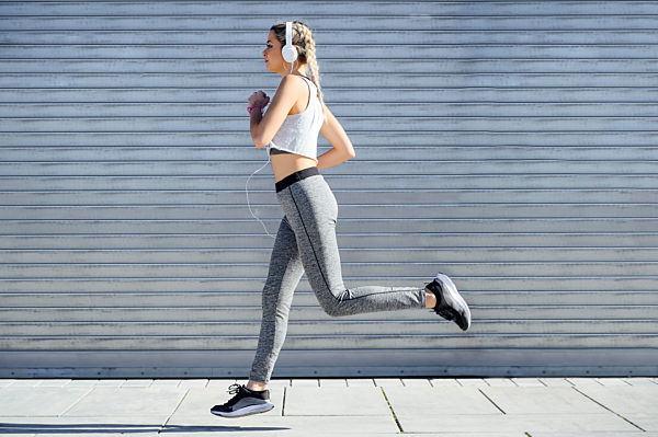 Female sportswoman wearing headphones running against shutter