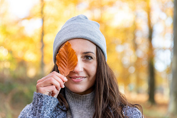 Beautiful woman covering eye with autumn leaf in Cannock Chase woodland