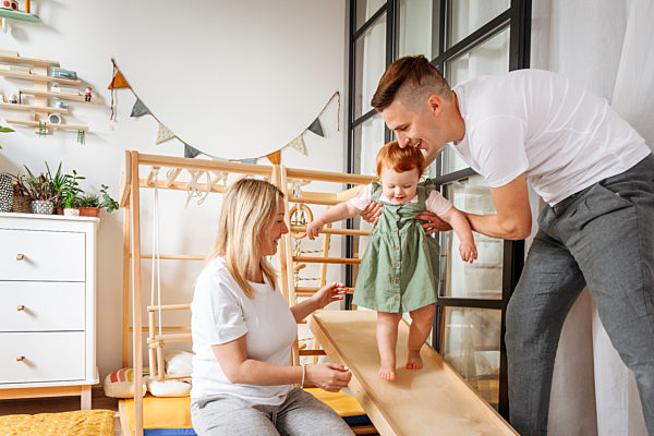 Parents assisting baby daughter walking at home