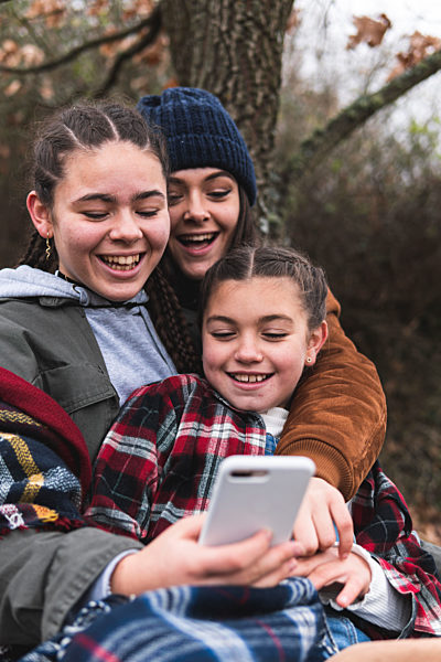 Three smiling sisters looking at smart phone in Autumn landscape