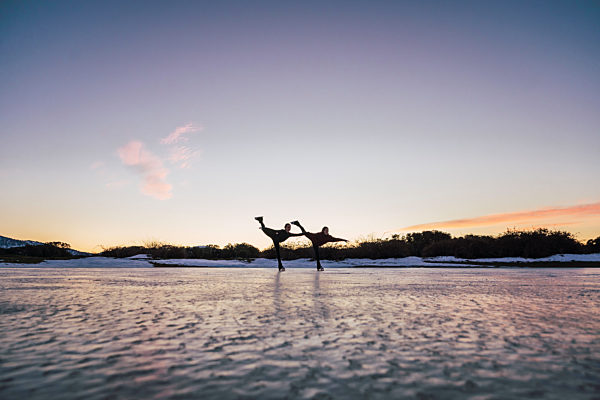 Silhouettes of two female figure skaters practicing together on frozen lake at dusk