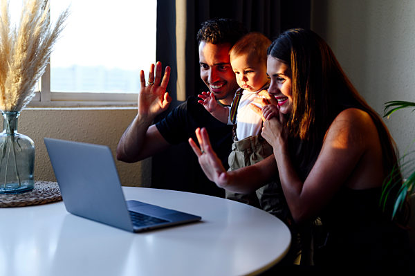 Smiling parents with son waving hand to video call while sitting at home