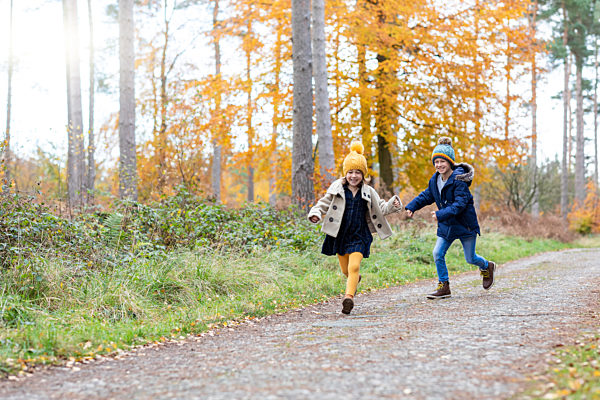 Cheerful siblings playing while running on forest path