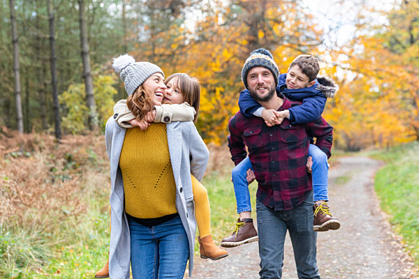 Parents piggybacking children while walking in forest during autumn