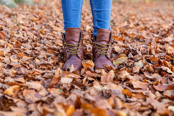 Woman in boots standing in autumn leaves while hiking in forest