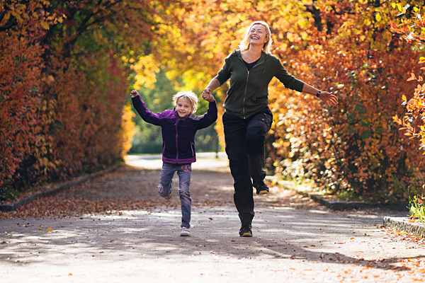 Mother and daughter holding hands and running in park during autumn