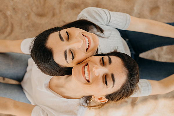 Smiling sisters with eyes closed on sand at beach