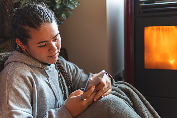 Teenage girl using mobile phone while sitting by fireplace at home