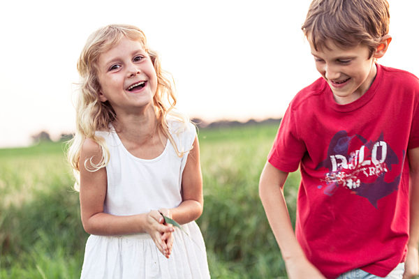 Cheerful cute girl standing by brother on green field