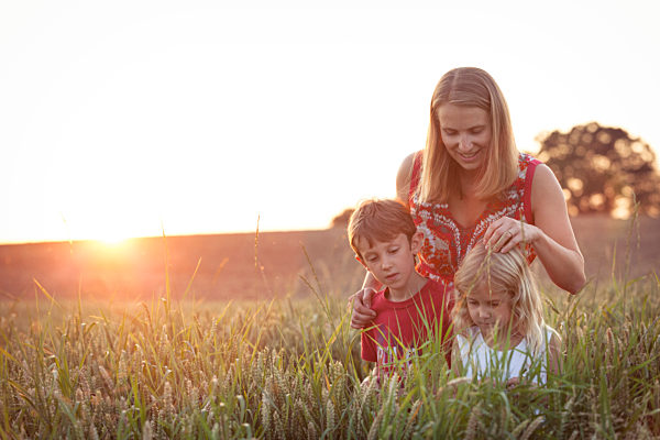 Boy and girl looking at plants in front of mother on agricultural field