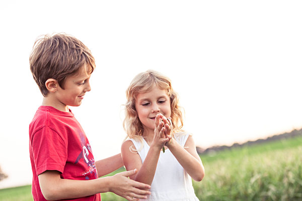 Smiling boy looking at sister playing with leaf in front of sky