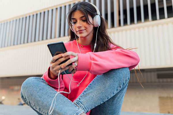Beautiful teenage girl wearing headphones while using smart phone