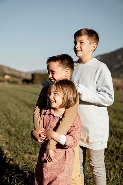 Smiling brothers and sister standing on agricultural field during sunny day