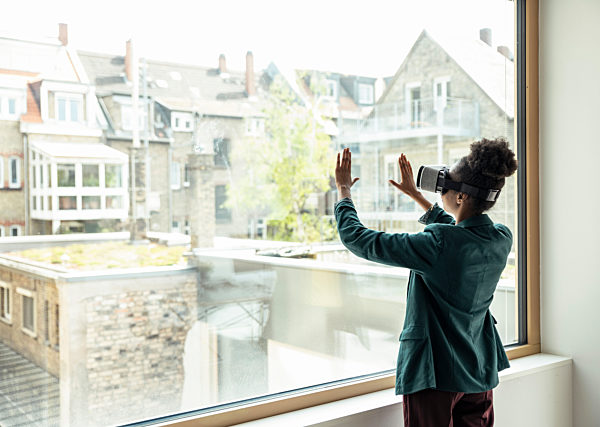 Female professional touching glass window while using virtual reality headset at office