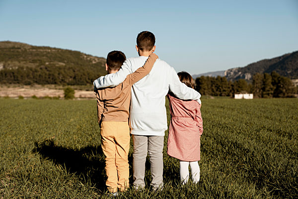 Brothers and sister standing with arms around on agricultural field
