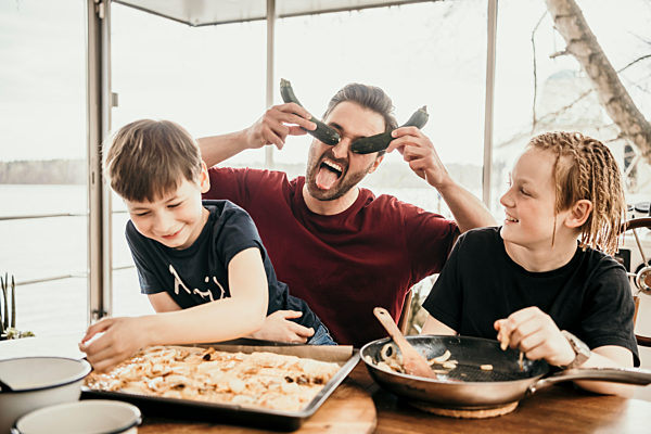 Playful father playing with sons while preparing food in kitchen at houseboat