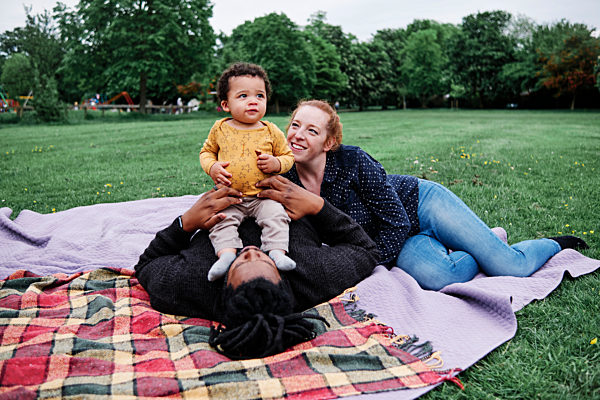 Happy family relaxing with son while lying on picnic blanket at park