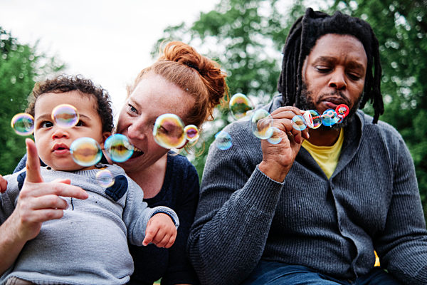 Father blowing bubbles while playing with family at park