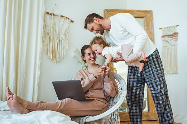 Smiling woman holding daughter's hand while carried by man at home