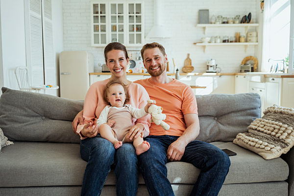 Smiling man and woman sitting on sofa with daughter on lap at home