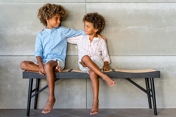 Boys with hand on shoulders looking at each other on bench