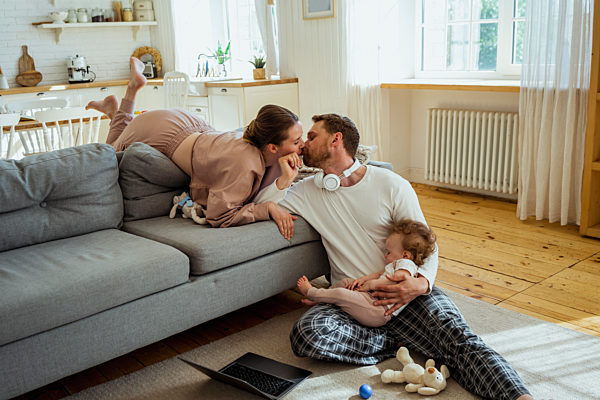 Woman kissing man while daughter sleeping on lap at home