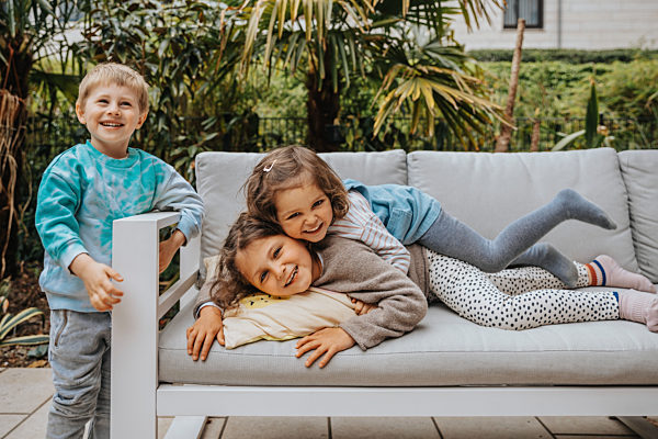 Boy standing by sofa while sisters enjoying at backyard