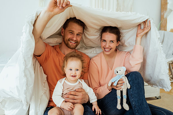 Smiling man and woman with daughter covered in blanket at home