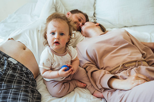 Cute daughter sitting amidst mother and father doing romance on bed at home