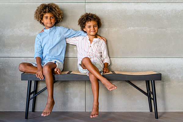 Boys with arm around sitting on bench at home