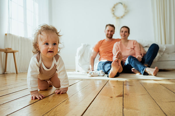 Cute girl crawling while mother and father sitting on floor at home