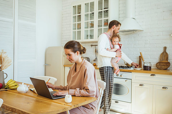 Businesswoman using laptop and man carrying daughter while preparing food at kitchen