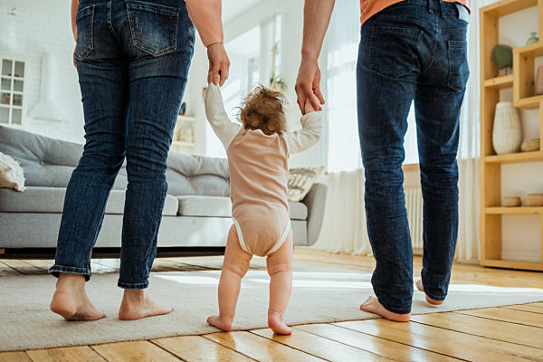 Baby girl holding hands of parents while walking in living room