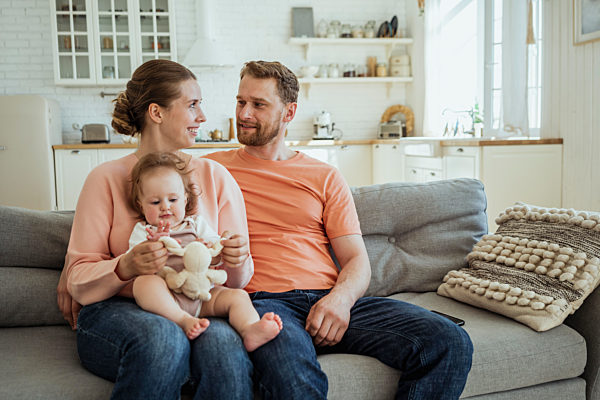Smiling woman with daughter on lap looking at man on sofa in living room