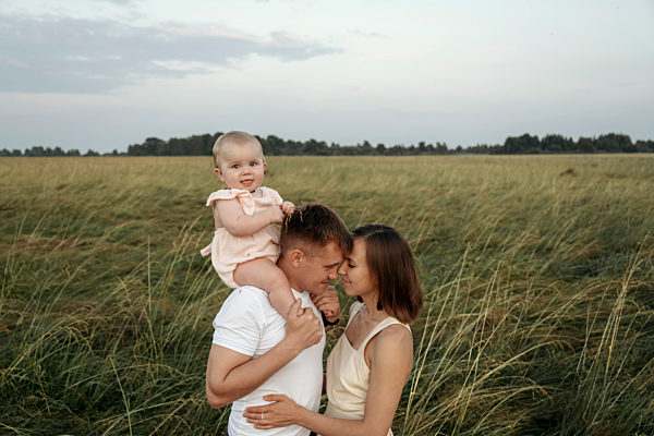 Affectionate parents embracing while carrying daughter on shoulders